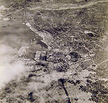 Black and white aerial photograph of a city. Part of the city at the bottom of the photograph has been completely destroyed.