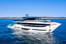 In the foreground, a large, white motor yacht on the sea, with an island in the background.