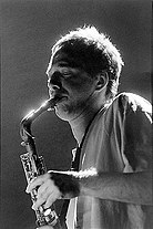 Black and white photo of a man with short hair and a T-shirt playing saxophone