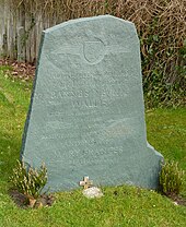 Irregular green gravestone standing in a grassy churchyard