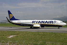 Avion blanc avec le bas-ventre noir, une harpe jaune sur la queue bleu marine de l'appareil. Il est sur une piste, le nez dirigé vers la droite de l'image.