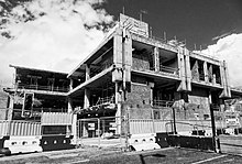 Black and white low level shot of part demolished modern building having a framework of exposed concrete pillars against a bright sky