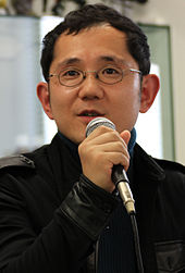 A 2011 photograph of Shu Takumi, holding a microphone.