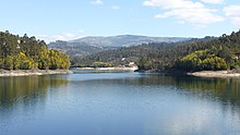 Panoramablick auf den Stausee und Talsperre in Farbe mit Berglandschaft und blauem Himmel am Horizont.