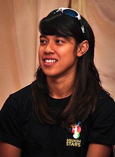 A women in a black t-shirt and a sunglasses on her head smiling.