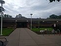 The facade of the St. Louis Park library, a one-story brick-and-concrete building with flowers lining the entry walkway. There is a bicycle rack off to the right.