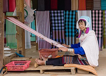 Mulher padaung com anéis decorativos no pescoço trabalhando em seu tear. Tachileik, Myanmar (Birmânia). O costume de usar anéis no pescoço está relacionado a um ideal de beleza: o pescoço alongado. Anéis de pescoço empurram a clavícula e as costelas para baixo. O alongamento do pescoço é principalmente ilusório. As vértebras cervicais não se alongam. Muitas vezes, considera-se que o turismo incentiva o uso de anéis de pescoço em Myanmar, pois são uma atração popular para os turistas. (definição 3 914 × 2 810)