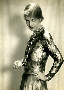 black and white photograph of a woman in a form fitting dress, holding a string of pearls in her hand looking over one shoulder.