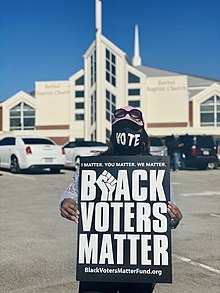 Woman holding a black sign with white lettering that reads "Black Voters Matter"