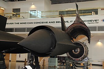 A view of the entry to an SR71 Mach 3.2 mixed external-internal inlet looking in direction of airflow to the engine. The centre translating cone has 26 inches of travel between extended, up to M1.6 (shown), and fully retracted at M3.2. An oblique shock from the cone tip, an internal oblique shock from the cowl lip and a normal shock[104] give the required pressure recovery at M3.2. The boundary layers on the cone and cowl inner surface have to be removed before the final shock-wave where the flow becomes subsonic. Otherwise shock-induced separation occurs. The two removal features are just visible. The cone boundary layer is removed through the band of holes (porous bleed). The boundary layer on the cowl inner surface is removed through a shock-trap[105] bleed. This ram bleed is just visible on the lower surface in front of a row of streamlined lumps called "mice" which reduce the rate of diffusion.[106]