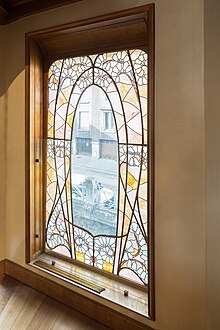 Verrière verticale parsemée de plombs courbes, dans le style "coup de fouet". Les verres sont translucides ou bien teintés en jaune. Permet de faire entrer la lumière dans une cage d'escalier en bois sombre Art nouveau.