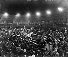 First sitting of Second Dáil in the Mansion House, 17 August 1921 (flopped image). In the un-flopped version of the photograph, sitting from left to right beside the Speaker's Chair are the Lord Mayor of Dublin, Seán T. O'Kelly, Éamon de Valera, Diarmuid O'Hegarty and F. P. Walsh, and sitting in front of the Speaker's Chair from left to right are Michael Collins and Richard Mulcahy.