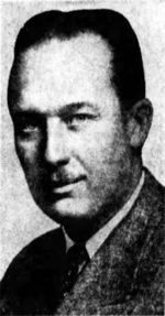 Black-and-white photographic portrait of a smiling adult man with slicked-back hair and a toothbrush mustache, wearing a suit. He eyes the camera with a classically handsome confidence.