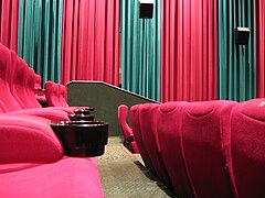 Interior of Hoyts cinemas auditorium in Perth, Australia, with stadium seating with cup holders, acoustic wall hangings and wall-mounted speakers.