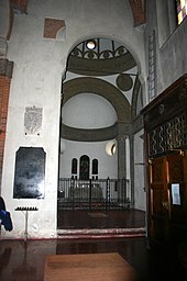 Photographie. Un intérieur d'église. Une chapelle en forme de fer à cheval. Murs blancs.