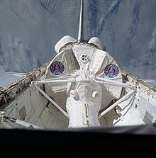 Columbia's open payload bay is visible above Earth. In the payload bay, a small white tunnel runs to a circular module.