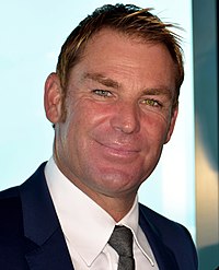 A man in cricket whites and hat. He is standing on steps of a stand.