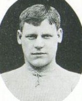 Head and shoulders of a young clean-shaven white man with neatly trimmed hair. He is looking straight ahead, and is wearing a shirt wth a drawstring at the neck.