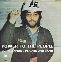 John Lennon wearing work clothing, aviator glasses, and a white hard helmet. His right hand is seen clenching a fist with his left hand behind him.