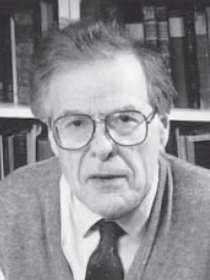 Photograph of Jones in later life, wearing glasses, a jumper and a tie, in front of his bookshelf