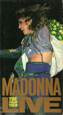 Madonna dancing while looking towards her right. She is clad in a brightly colored jacket and a purple skirt, with a crucifix hanging from her neck.