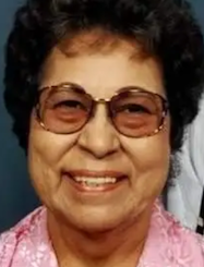 A smiling older Native American woman wearing glasses and a pink shirt