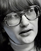 Closeup of a white woman's face; she is wearing glasses and her dark hair is cut in long bangs.