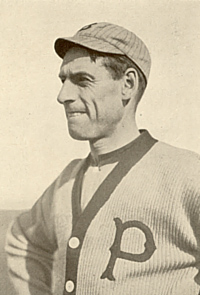 A sepia-toned image of a man wearing a button-down sweater with a "P" on the left breast and a crownless pinstriped baseball cap