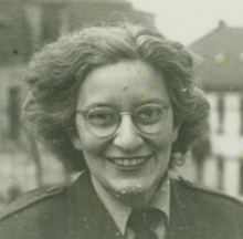 a black and white headshot of a woman staring into the camera, she has round glasses and dark wavy hair