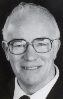 Black and white photo of an elderly white-haired man in a suit and tie wearing eyeglasses