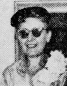 A smiling, slim white woman wearing a hat, sunglasses and a corsage, from a 1955 newspaper photo