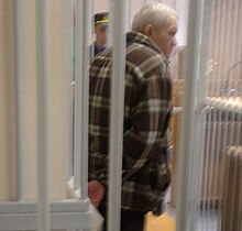 A slouching Lykov in a courtroom with handcuffs, facing away from the camera