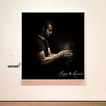 A photo of a man in a black shirt against a black background hanging in an art gallery