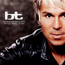A close-up shot of BT covers half of his face from the right side of the cover, as he is positioned in front of a brown background. BT is wearing a black leather jacket while his hair is white and brown. The artist name and song title is written in white text on the left side of the cover.