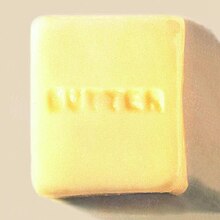 A photograph of a square of butter with the word "butter" carved into it in all caps.