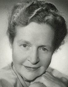 Publicity shot of smiling woman, wearing a light lipstick, with her hair Marcel-waved and pinned up (not bobbed yet).