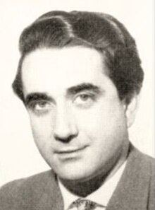 Glamour publicity shot of clean-shaven, half-smiling young man in suit and tie, with dark eyebrows, swept-back black hair and strong features.