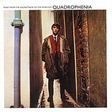 Square white and colour printed illustration for the commercially available soundtrack recording showing actor Phil Daniels standing in a narrow tall alleyway dressed in smart mod attire similar to that he wore as lead actor in the Quadrophenia film during a scooter trip to Brighton including shirt, tie and green army style parka