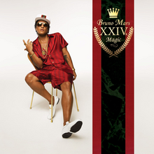 A man sitting on a gold chair with two fingers of his right hand up and his left hand down, wearing a white cap, red shirt and shorts. On the right of the image a red and black strip displays a crown and the words XXIVK Magic and Bruno Mars