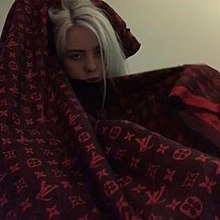 The cover features Eilish wrapped around in a blanket