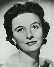 1950s-style full-face publicity shot of dark-haired young woman with 1950s soft perm, heavy make-up and clip-on earrings.