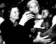 Two women holding an orphan who is being bottle-fed