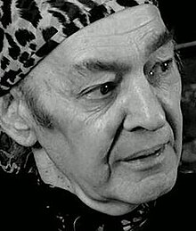 Three-quarter view of man with strong features, wearing a tigerskin-print headscarf, tied at the back
