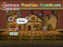 Mario with a goomba on a stage with cardboard, run-down buildings in the background. To the far right is Gus, a turtle-like creature, the current enemy they are fighting.
