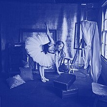 A photo, recolored blue, of the artist in a ballerina outfit doing stretches.