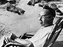 A black-and-white portrait of a seated man with a cigarette