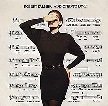 A model with a hand raised covering her eyes, her other hand is on her hip. She is wearing a black dress and dark tights. Her face is heavy with makeup, the white of her face contrasting dramatically with her red lips. The background is a filled by a sheet of music notation.