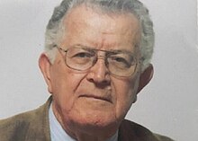 a colour headshot of a grey-haired man wearing glasses