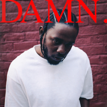 Kendrick Lamar dressed in a off-white shirt behind red bricks. The word "DAMN." appears on the top in red.