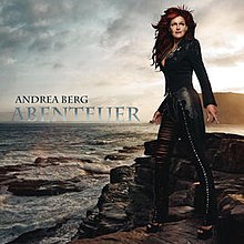 A red-haired woman dressed in black is looking in the distance. She is standing on a cliff and the sea can be seen in the background. The words "Andrea Berg Abenteuer" are written above the horizon line.